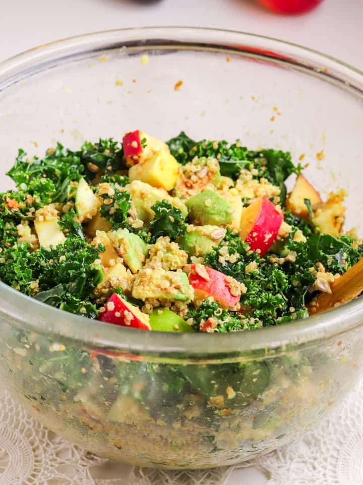 Tossing Kale quinoa salad with apples in a glass bowl