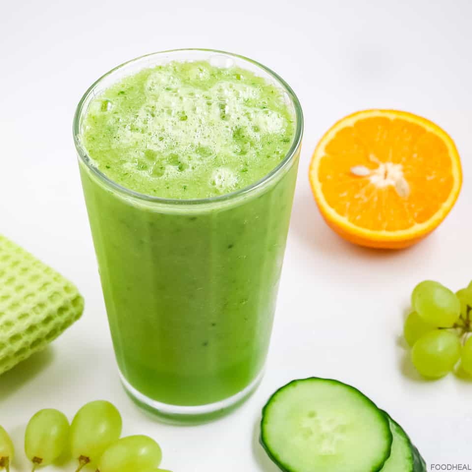 a glass of cucumber smoothie with sliced cucumbers, orange and green grapes