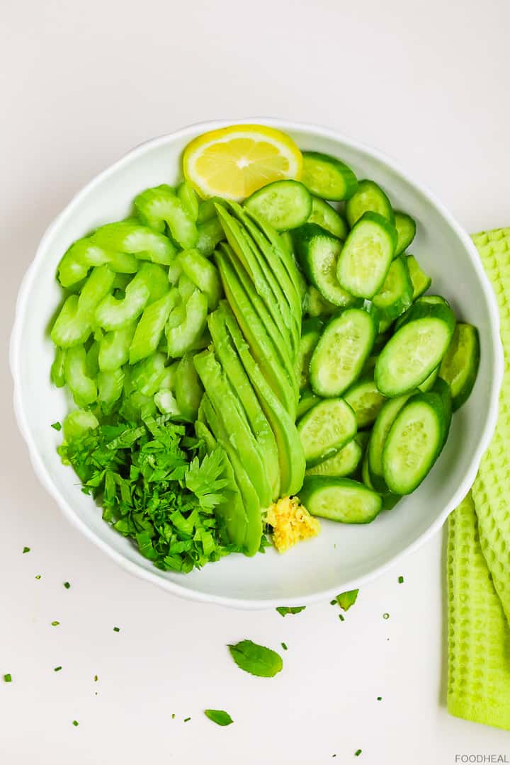 Sliced cucumber, avocado, celery, lemon, & ginger in a salad bowl